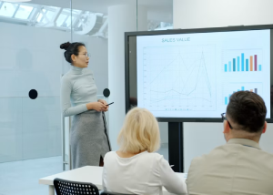 Woman presenting sales data on a screen to seated colleagues